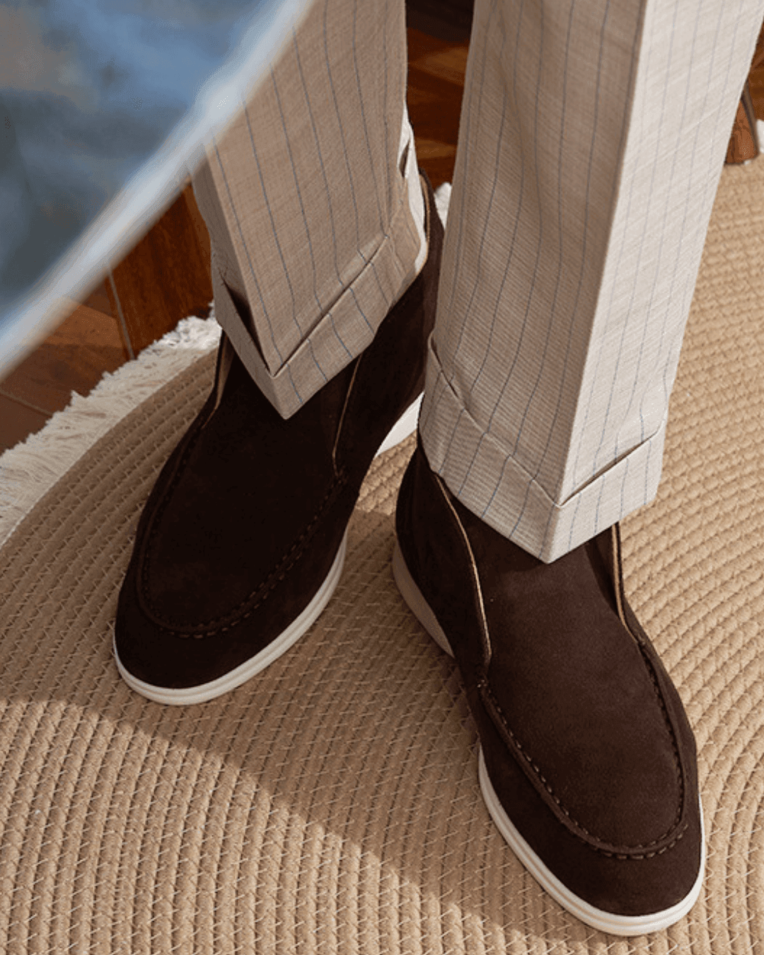 Brown suede shoes worn with light-colored pants on a textured surface