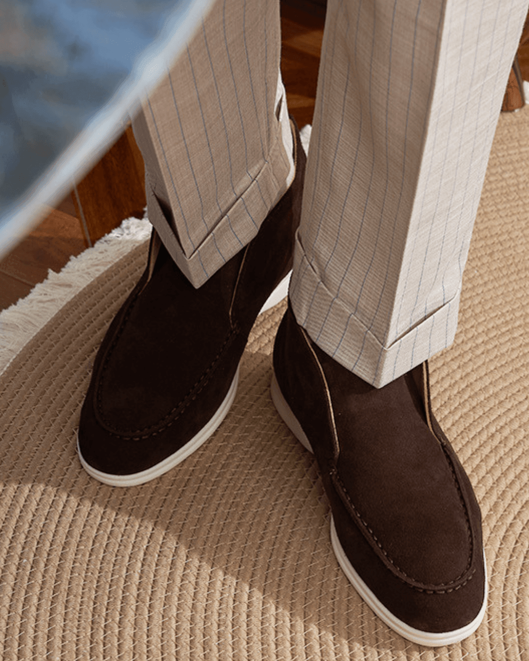 Brown suede shoes worn with beige pants on a carpeted floor.