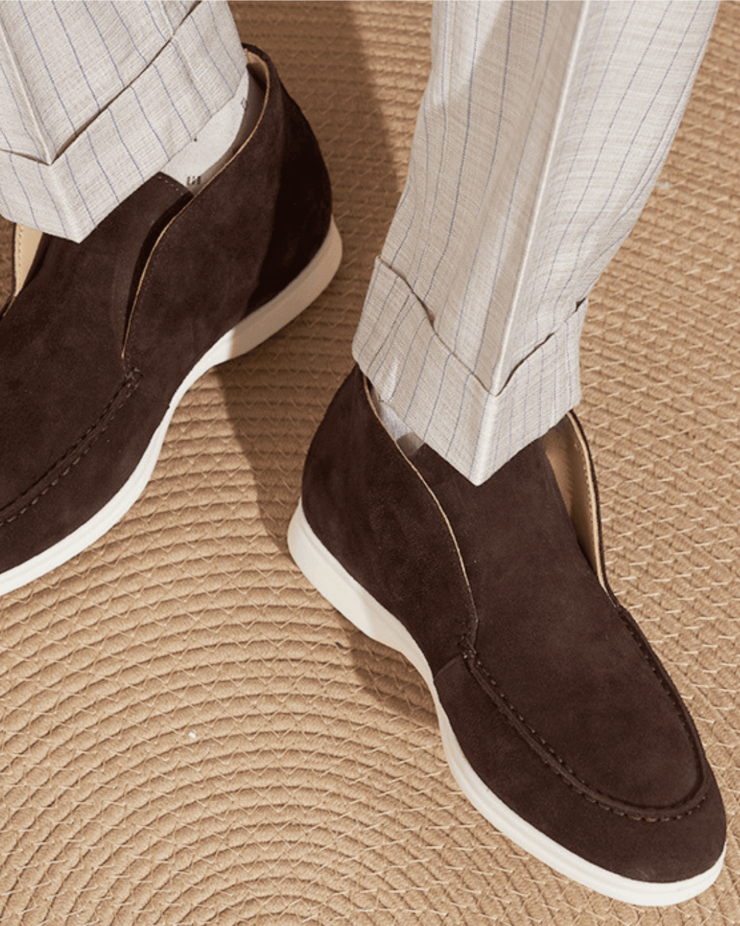Brown suede loafers worn with light-colored pants on a textured surface